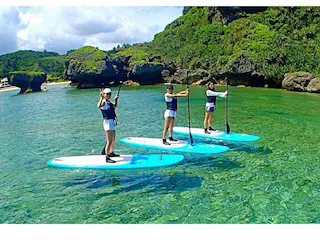 4名で沖縄の綺麗な海でSUPを楽しんでいる"